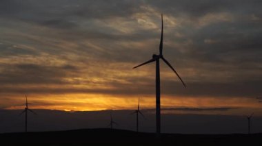 Bir tarladaki büyük bir rüzgar türbininin pervanelerini ufuktaki turuncu günbatımının arka planına doğru hareket ettir. Alternatif enerji kaynakları. Rüzgarlı park. Ekolojik enerji. Sanayi.