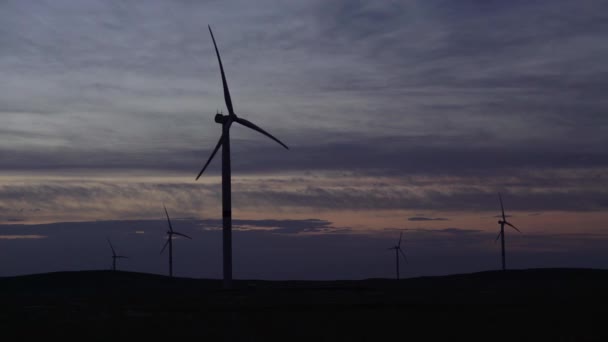 Movimiento de las palas de un gran aerogenerador en un campo sobre un fondo de puesta de sol en el horizonte con una hermosa colinas. Fuentes de energía alternativas. Parque de viento. Energía ecológica.Industrial — Vídeos de Stock