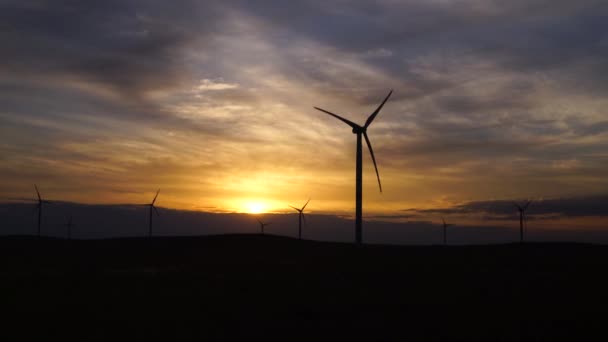 Bir tarladaki büyük bir rüzgar türbininin pervanelerini ufuktaki turuncu günbatımının arka planına doğru hareket ettir. Alternatif enerji kaynakları. Rüzgarlı park. Ekolojik enerji. Sanayi. — Stok video