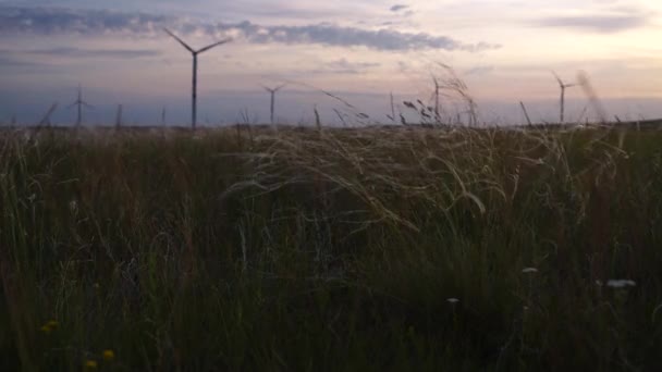 Movimiento de las palas de un gran aerogenerador en un campo sobre un fondo de naranja puesta de sol en el horizonte con una hermosa colinas. Fuentes de energía alternativas. Parque de viento. Energía ecológica.Industrial — Vídeos de Stock