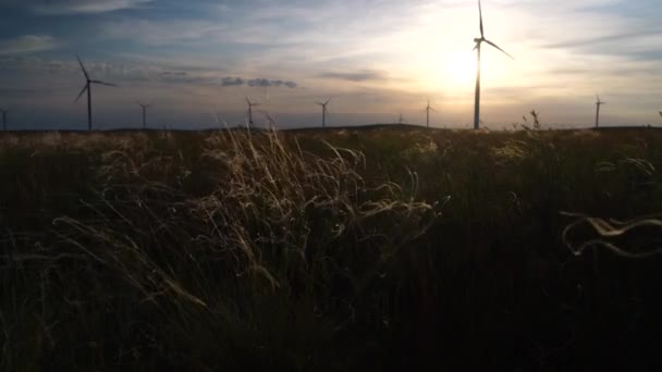 Poruszaj ostrzami dużej turbiny wiatrowej w polu na tle pomarańczowego zachodu słońca na horyzoncie z pięknymi wzgórzami. Alternatywne źródła energii. Park wiatrów. Energia ekologiczna.Przemysł — Wideo stockowe