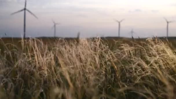 Poruszaj ostrzami dużej turbiny wiatrowej w polu na tle pomarańczowego zachodu słońca na horyzoncie z pięknymi wzgórzami. Alternatywne źródła energii. Park wiatrów. Energia ekologiczna.Przemysł — Wideo stockowe