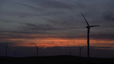 Bir tarladaki büyük bir rüzgar türbininin pervanelerini ufuktaki turuncu günbatımının arka planına doğru hareket ettir. Alternatif enerji kaynakları. Rüzgarlı park. Ekolojik enerji. Sanayi.