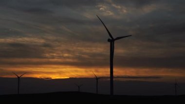Bir tarladaki büyük bir rüzgar türbininin pervanelerini ufuktaki turuncu günbatımının arka planına doğru hareket ettir. Alternatif enerji kaynakları. Rüzgarlı park. Ekolojik enerji. Sanayi.