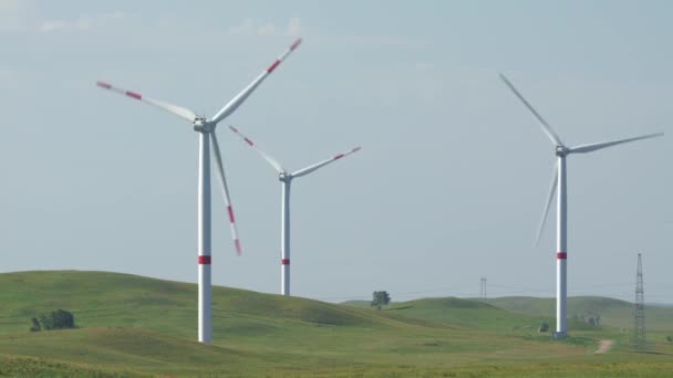 Mova as lâminas de uma grande turbina eólica em um campo contra um fundo de céu azul nublado com grama de penas balançando ao vento. Fontes de energia alternativas. Parque ventoso. Energia ecológica. — Vídeo de Stock