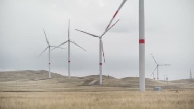 Ufukta bulutlu gri gökyüzü ve güzel tepeleri olan bir tarladaki büyük bir rüzgar türbininin kanatlarını hareket ettir. Alternatif enerji kaynakları. Rüzgarlı park. Ekolojik enerji. Sanayi.