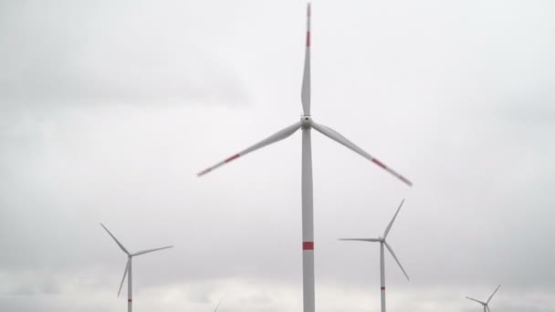 Motion the blades of a large wind turbine in a field against a background of cloudy grey sky on the horizon with a beautiful hills. Alternative energy sources. Windy park. Ecological energy.Industrial — Stock Video
