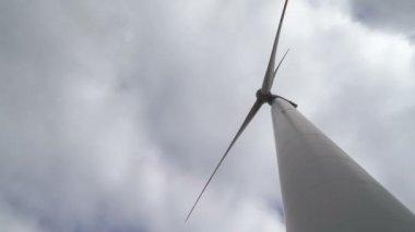 Ufukta bulutlu gri gökyüzü ve güzel tepeleri olan bir tarladaki büyük bir rüzgar türbininin kanatlarını hareket ettir. Alternatif enerji kaynakları. Rüzgarlı park. Ekolojik enerji. Sanayi.