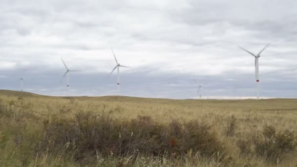 Motion the blades of a large wind turbine in a field against a background of cloudy grey sky on the horizon with a beautiful hills. Alternative energy sources. Windy park. Ecological energy.Industrial — Stock Video