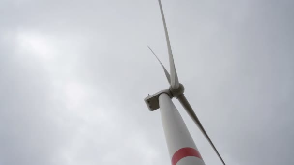 Beweeg de bladen van een grote windturbine in een veld tegen een achtergrond van bewolkte grijze lucht aan de horizon met een prachtige heuvels. Alternatieve energiebronnen. Winderig park. Ecologische energie.Industrieel — Stockvideo