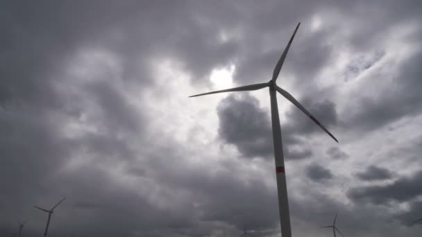 Rörelse bladen av en stor vindturbin i ett fält mot en bakgrund av molnig grå himmel på horisonten med en vacker kullar. Alternativa energikällor. Blåsig park. Ekologisk energi.Industriell — Stockvideo