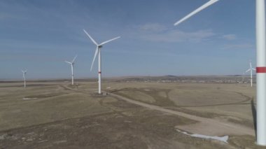 Ufukta bulutlu mavi gökyüzü ve güzel tepeleri olan bir tarladaki büyük bir rüzgar türbininin bıçakları. Alternatif enerji kaynakları. Rüzgarlı park. Ekolojik enerji. Sanayi.