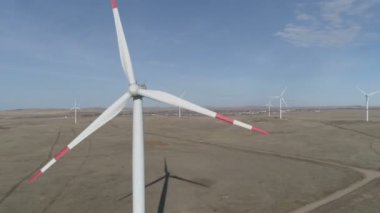 Ufukta bulutlu mavi gökyüzü ve güzel tepeleri olan bir tarladaki büyük bir rüzgar türbininin bıçakları. Alternatif enerji kaynakları. Rüzgarlı park. Ekolojik enerji. Sanayi.