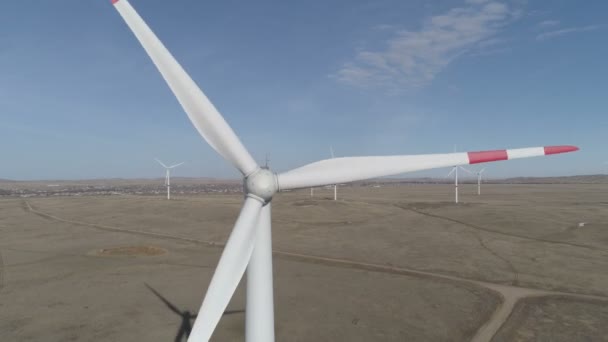 Ufukta bulutlu mavi gökyüzü ve güzel tepeleri olan bir tarladaki büyük bir rüzgar türbininin bıçakları. Alternatif enerji kaynakları. Rüzgarlı park. Ekolojik enerji. Sanayi. — Stok video