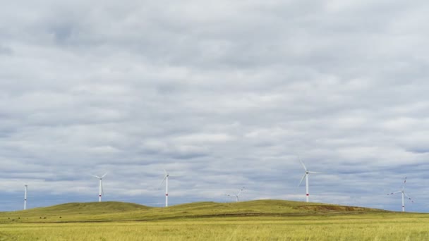 Blad av en stor vindkraftverk i ett fält mot en bakgrund av molnigt blå himmel på horisonten med en vacker kullar. Alternativa energikällor. Blåsig park. Ekologisk energi.Industriell — Stockvideo