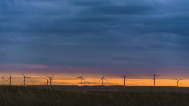 Bewegen Sie die Flügel einer großen Windkraftanlage auf einem Feld vor dem Hintergrund eines orangefarbenen Sonnenuntergangs am Horizont mit einem wunderschönen Hügel. Alternative Energiequellen. Windiger Park. Ökologische Energie.Industrie — Stockvideo