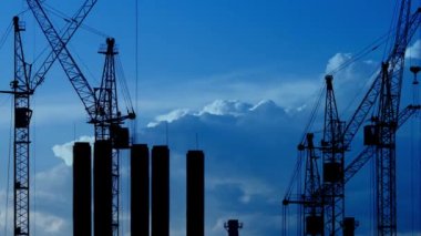 Şantiye alacakaranlıkta, mor gökyüzü ile birlikte. Yüksek kule vinçlerinin silueti yüksek katlı konut sahasında çalışır, yük kaldırır.