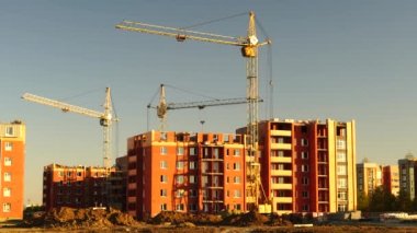 Şantiye turuncu gün batımında. Yüksek kule vinçlerinin silueti yüksek katlı konut sahasında çalışır, yük kaldırır.