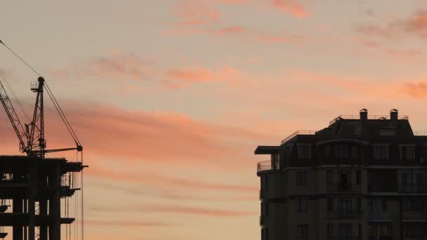 Baustelle bei orangenem Sonnenuntergang. Silhouette hoher Turmdrehkrane arbeitet auf Wohnhochhaus-Baustelle, hebt Last. — Stockvideo