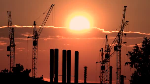 Baustelle bei orangenem Sonnenuntergang. Silhouette hoher Turmdrehkrane arbeitet auf Wohnhochhaus-Baustelle, hebt Last. — Stockvideo