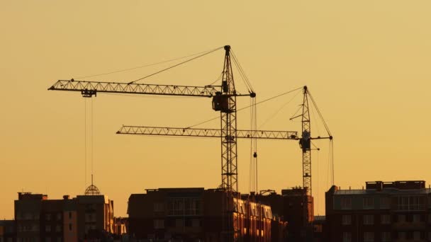 Baustelle bei orangenem Sonnenuntergang. Silhouette hoher Turmdrehkrane arbeitet auf Wohnhochhaus-Baustelle, hebt Last. — Stockvideo