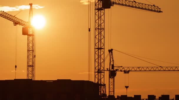 Cantiere al tramonto arancione. La sagoma di gru a torre alte lavora in cantiere residenziale a molti piani, solleva il carico. — Video Stock