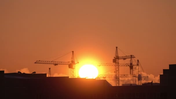 Şantiye turuncu gün batımında. Yüksek kule vinçlerinin silueti yüksek katlı konut sahasında çalışır, yük kaldırır. — Stok video