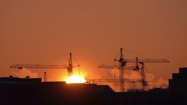 Bouwplaats bij oranje zonsondergang. Silhouet van hoge torenkranen werkt op hoogbouw, liften belasting. — Stockvideo