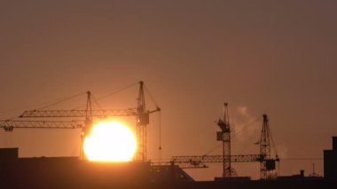 Şantiye turuncu gün batımında. Yüksek kule vinçlerinin silueti yüksek katlı konut sahasında çalışır, yük kaldırır.