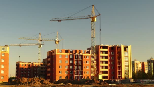 Staveniště při oranžovém západu slunce. Silueta jeřábů s vysokými věžemi pracuje na vysokohorské rezidenční stavbě, zatížení výtahů. — Stock video