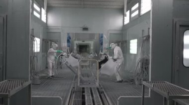 Koşu bandındaki araç parçalarını boyamak. Araba üretim fabrikası. İki ressam çarpışan bir arabaya beyaz boya sıkarlar..
