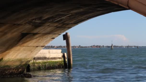 Blick unter einer Steinbrücke auf die Lagune von Venedig, Italien. heller Himmel und blaues Wasser mit sanften Wellen. — Stockvideo