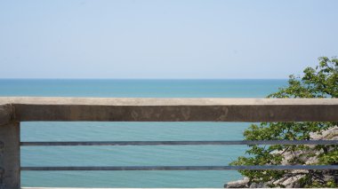Balkon korkuluk beton ve Metal mavi okyanus yukarıda ve mavi Bulutsuz gökyüzü önünde yaptı. Sağ tarafında bazı yeşil bitkiler.