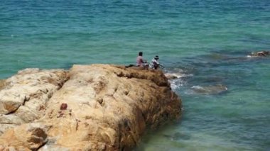Kahverengi bir kayaya denize oturan iki kimliği belirsiz balıkçı