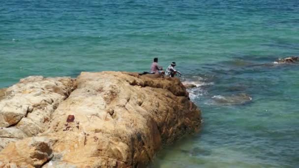 Dois pescadores não identificados sentados numa rocha castanha no mar — Vídeo de Stock