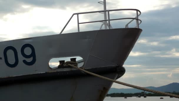 Bow of white ship tied down to the dock in the harbor by thick rope. Moored boat in front of sea and cloudy sky. — Stock Video