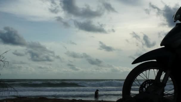 Silhuett av framhjulet för motorcykel vid stranden med kvinna på stranden — Stockvideo