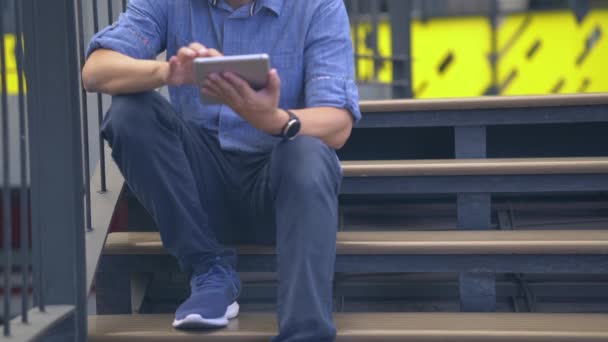 Mann Sitzt Auf Der Treppe Und Spricht Auf Dem Tablet — Stockvideo