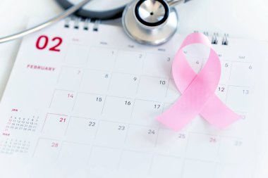 Kanser Günü konsepti: Siyah taş tahtada göğüs kanseri ve takvimin pembe kurdele sembolü
