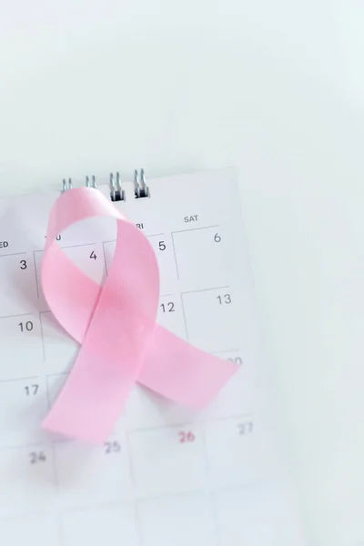 Cancer day concept : Pink ribbon symbol of breast cancer and calendar on black stone board background