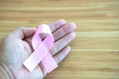 Ahşap arka planda pembe kurdeleler tutan eller, göğüs kanseri farkındalığı ve Şubat kanser günü konsepti 