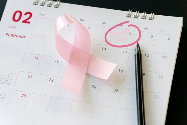 Cancer day concept : Pink ribbon symbol of breast cancer and calendar background