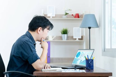 İşadamı dizüstü bilgisayarı üzerinde çalışıyor. Verileri ve grafiği analiz eden, dizüstü bilgisayarda yazı yazan genç adam tahta masada oturuyor..