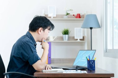 E öğrenme konsepti. Sıradan bir iş adamı evdeki dizüstü bilgisayarında çalışıyor. Adam dizüstü bilgisayarla çevrimiçi kurs ve not defteri üzerine ders çalışıyor..