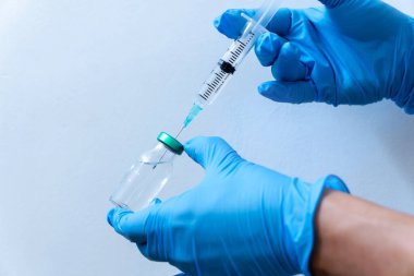 Mavi arka planda izole edilmiş: doktorun eldivenli eli virüs kavramına karşı bir şırınga aşısı tutuyor.