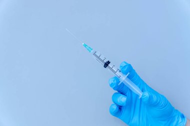 Mavi arka planda izole edilmiş: doktorun eldivenli eli virüs kavramına karşı bir şırınga aşısı tutuyor