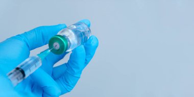 Mavi arka planda izole edilmiş: doktorun eldivenli eli virüs kavramına karşı bir şırınga aşısı tutuyor.
