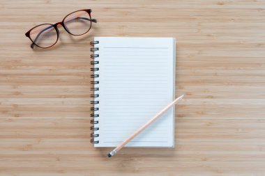 Not defteri, gözlük ve kalem açık tahta masa arka planında. Metnin için alanı kopyala. Düz yatıyordu.