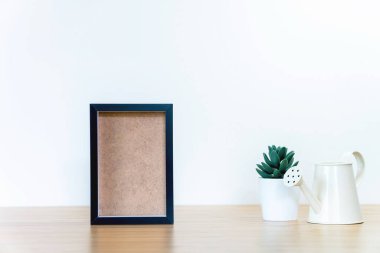 siyah kare çerçeveler ve ahşap masa üzerindeki yeşil bitki, boş çerçeveler