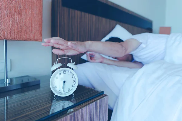 Yatakta uzanmış, elini kapatmış, çalar saat rengine uzanmış siyah bir adam. Sabah 6: 30 'da uyanır..